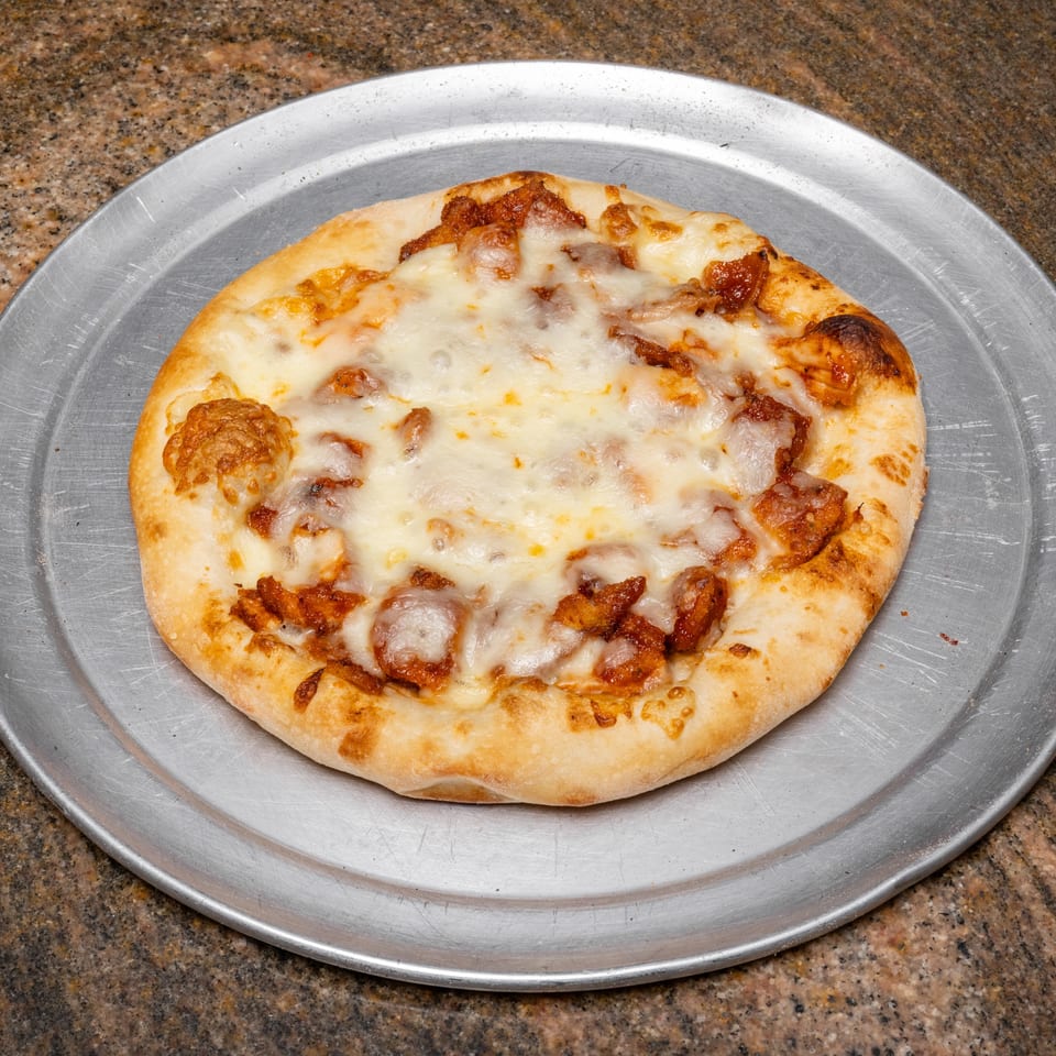 A small, round pizza with melted cheese and chicken pieces on a metal tray.