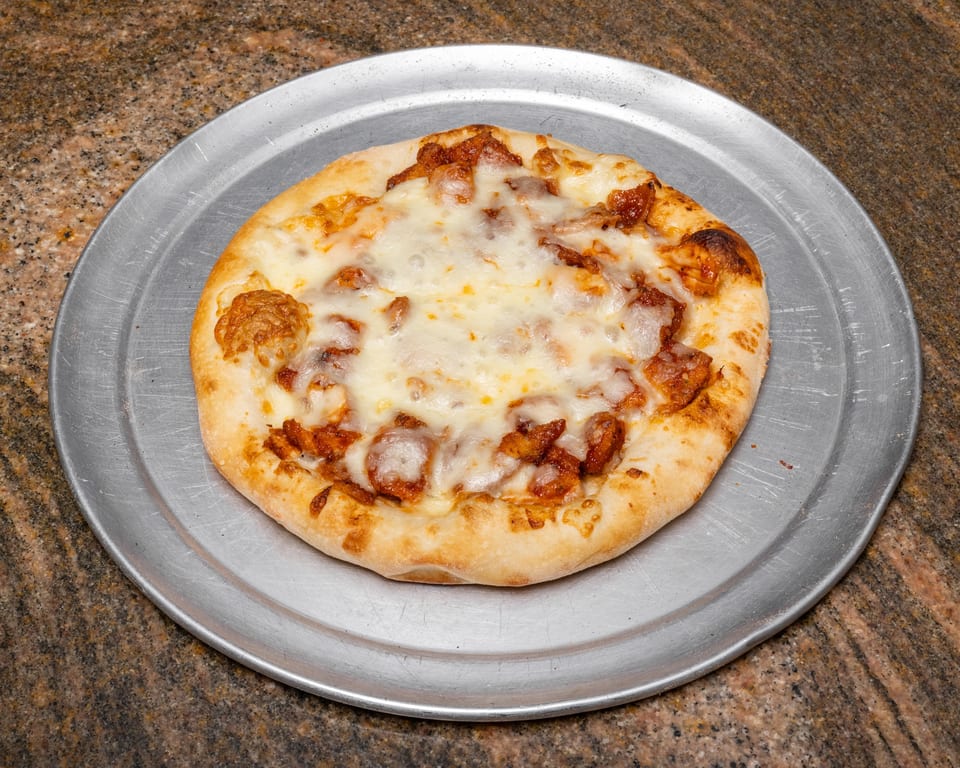 A small, round pizza with melted cheese and chicken pieces on a metal tray.