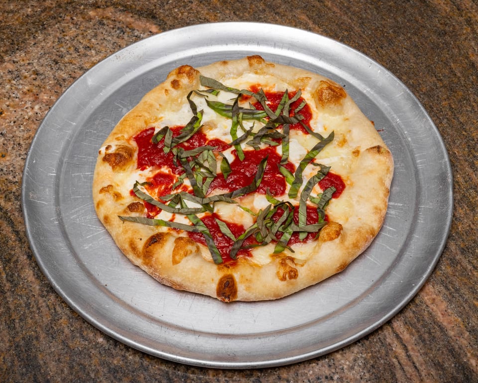 A freshly baked Margherita pizza with tomato sauce, mozzarella, and basil on a metal tray.