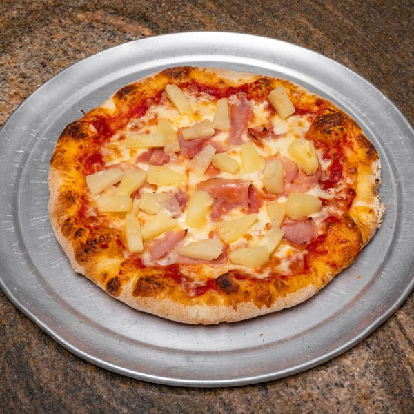 A Hawaiian pizza with ham and pineapple on a metal tray, on a granite countertop.