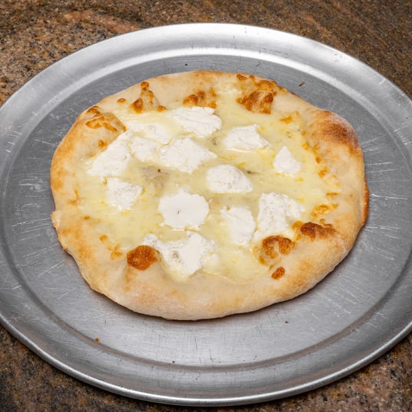 A small white pizza with ricotta cheese dollops and melted mozzarella on a metal pan.
