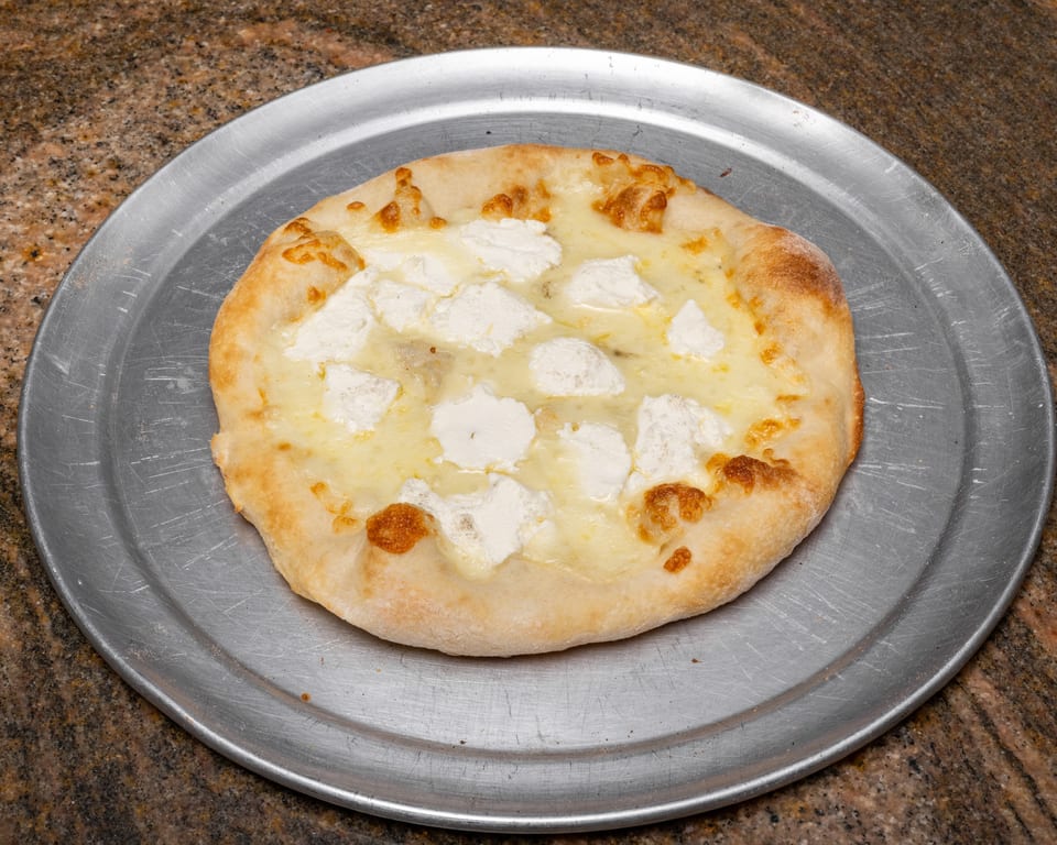 A small white pizza with ricotta cheese dollops and melted mozzarella on a metal pan.