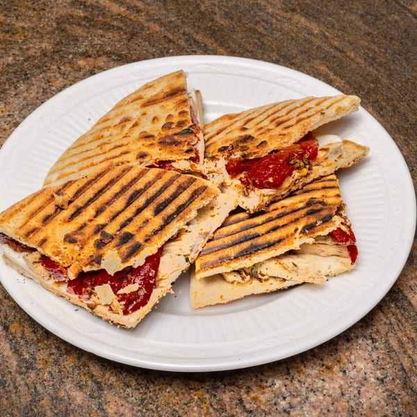 Grilled panini sandwiches with chicken, red peppers, and cheese, cut into quarters on a white plate.