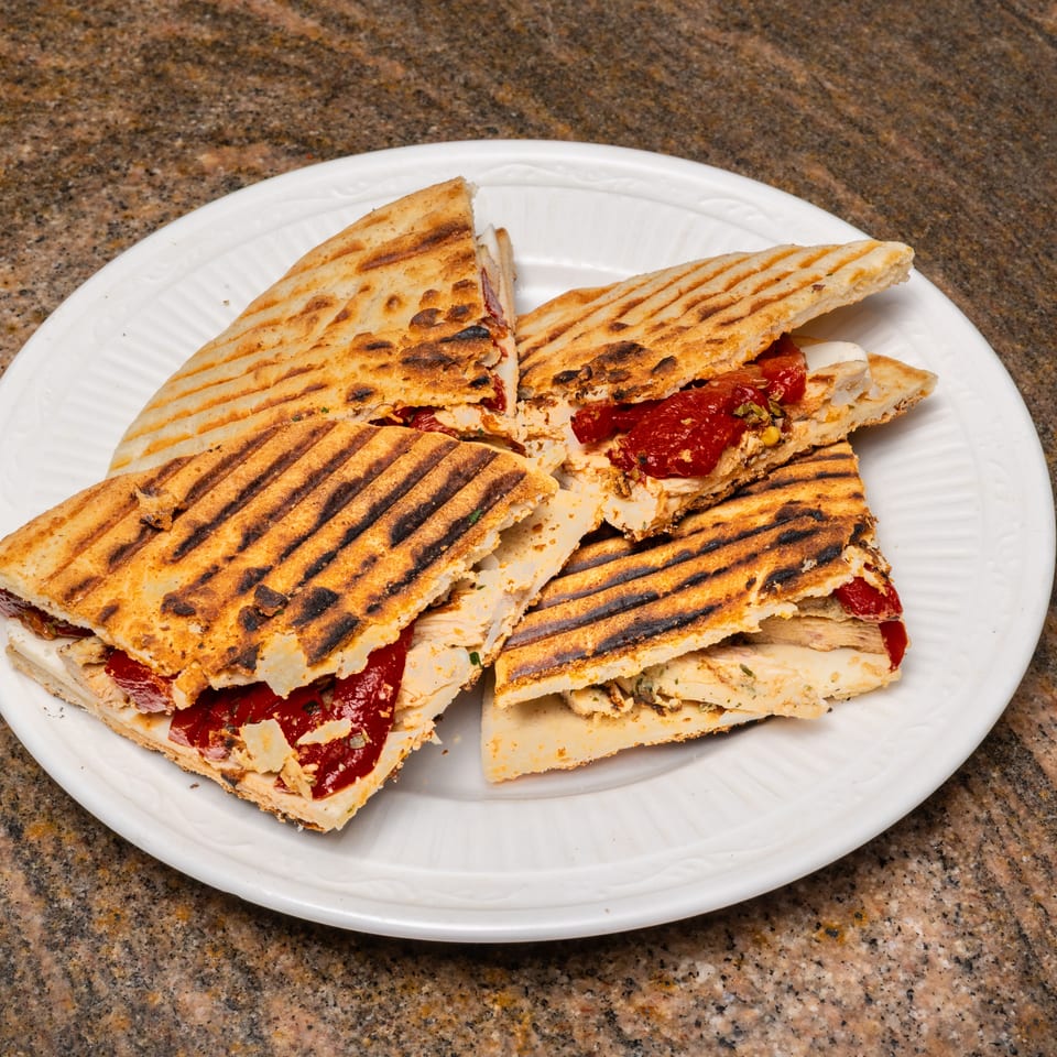 Grilled panini sandwiches with chicken, red peppers, and cheese, cut into quarters on a white plate.