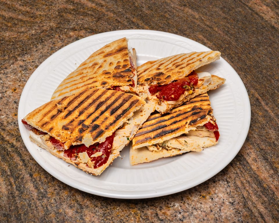 Grilled panini sandwiches with chicken, red peppers, and cheese, cut into quarters on a white plate.