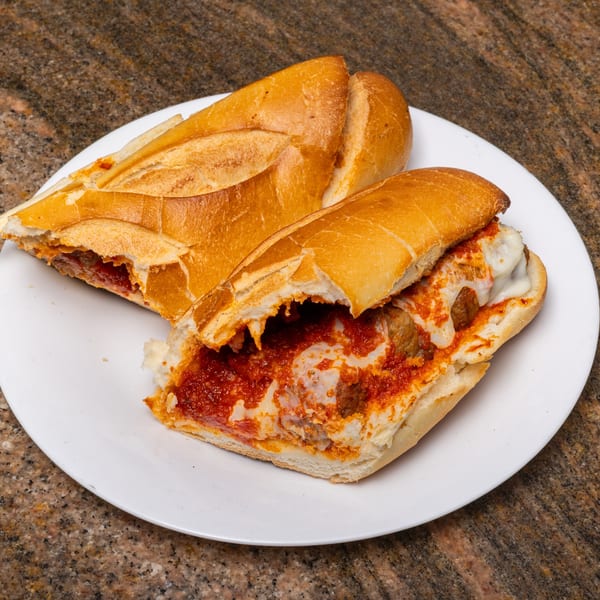 Two halves of a meatball sub sandwich with melted cheese and red sauce on a white plate.