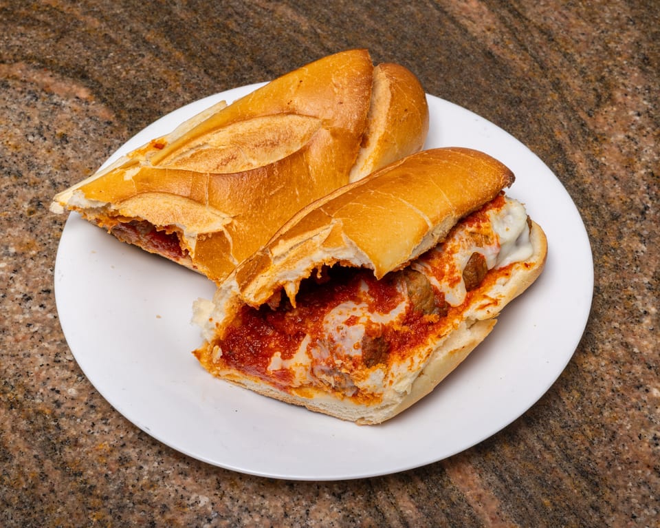 Two halves of a meatball sub sandwich with melted cheese and red sauce on a white plate.