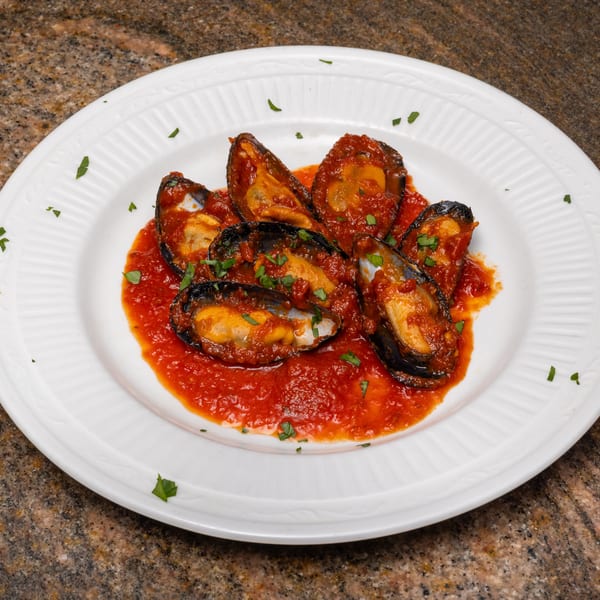 Mussels in red sauce with parsley on a white plate.