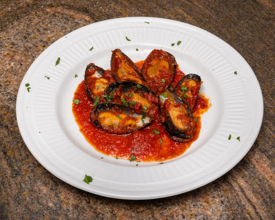 Mussels in red sauce with parsley on a white plate.