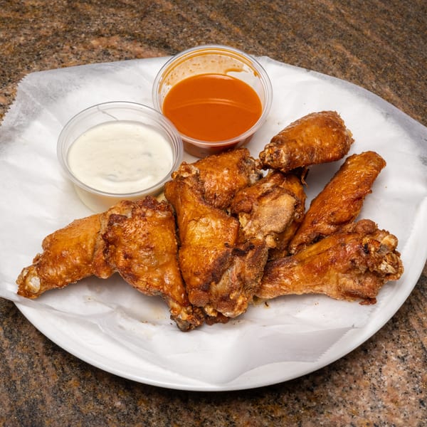 Crispy fried chicken wings on a white plate with ranch and hot sauce dips.