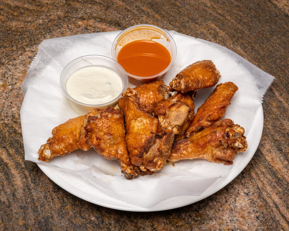 Crispy fried chicken wings on a white plate with ranch and hot sauce dips.